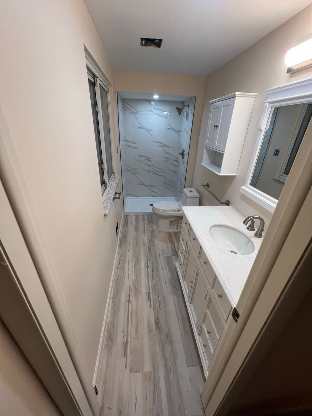 Finished bathroom remodel in Metro Detroit with a custom marble-look tile shower, new vanity, and plank flooring